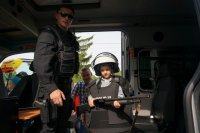 Dzieci przymierzają w radiowozie policyjną kamizelkę przeciwuderzeniową i kask.