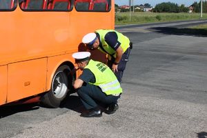 umundurowany policjant wraz inspektorem transportu drogowego kontrolują ogumienie autobusu