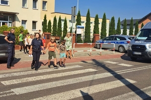 Zdjęcie przedstawia policjantkę oraz dzieci przechodzące przez oznakowane przejście dla pieszych.