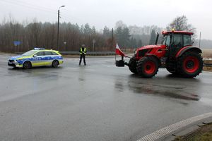 Zdjęcie przedstawia umundurowanych policjanta kierującego ruchem, oznakowany radiowóz oraz ciągniki rolnicze.